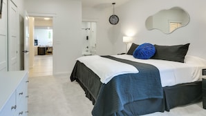 Une chambre à coucher comprenant un lit, des tables de chevet, une commode, un miroir et un luminaire suspendu.