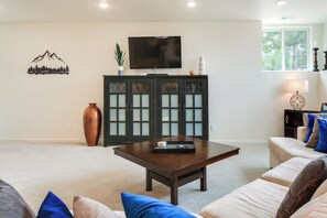 Un salon comprenant un téléviseur à écran plat, un meuble avec des portes en verre dépoli, une table basse et un canapé avec des coussins.