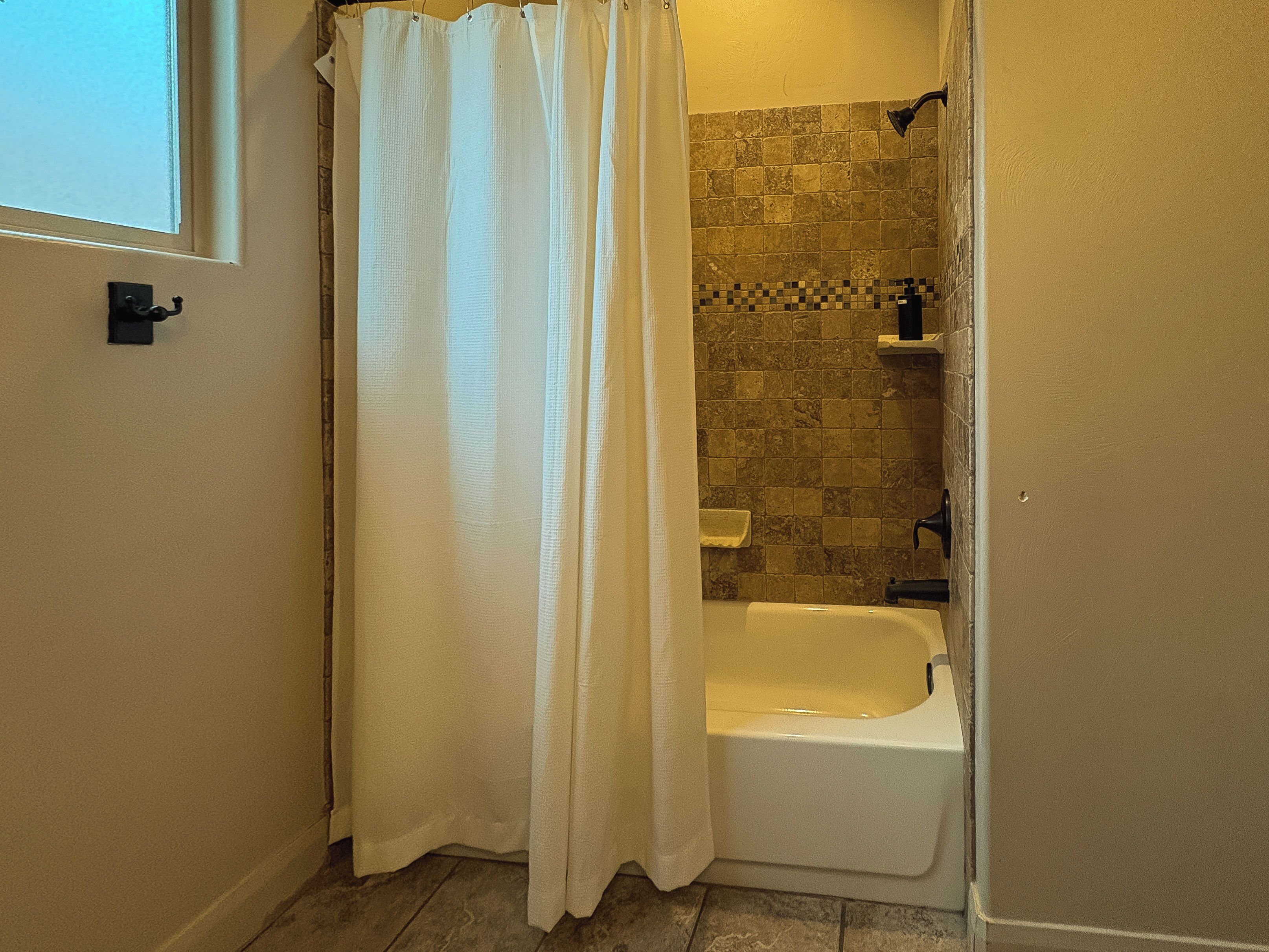 Un baño con ducha, bañera y pared de azulejos.