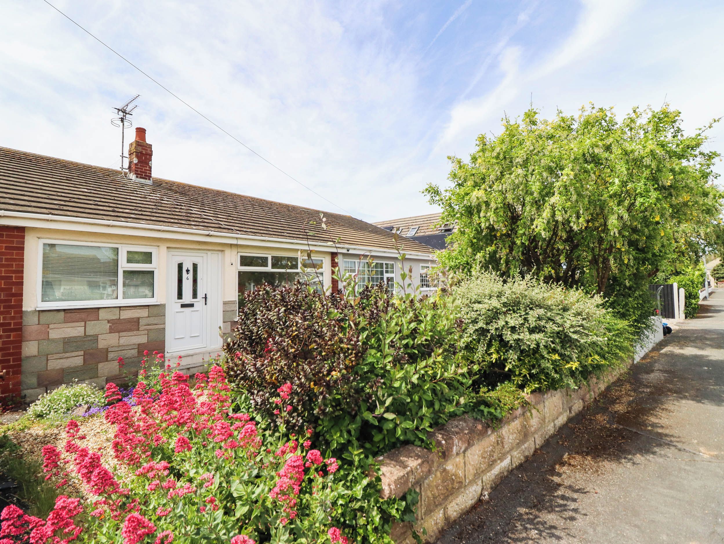 A residential property with a brick facade, a white door, and a garden with flowering plants.
