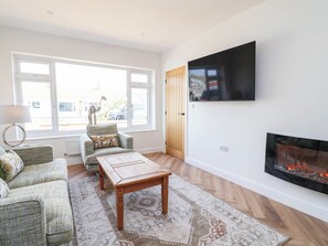 Una sala de estar con chimenea, televisor montado en la pared, sofá, sillón y alfombra estampada.