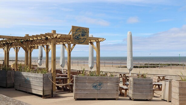 Un café de madera frente a la playa con terraza y vistas al océano.