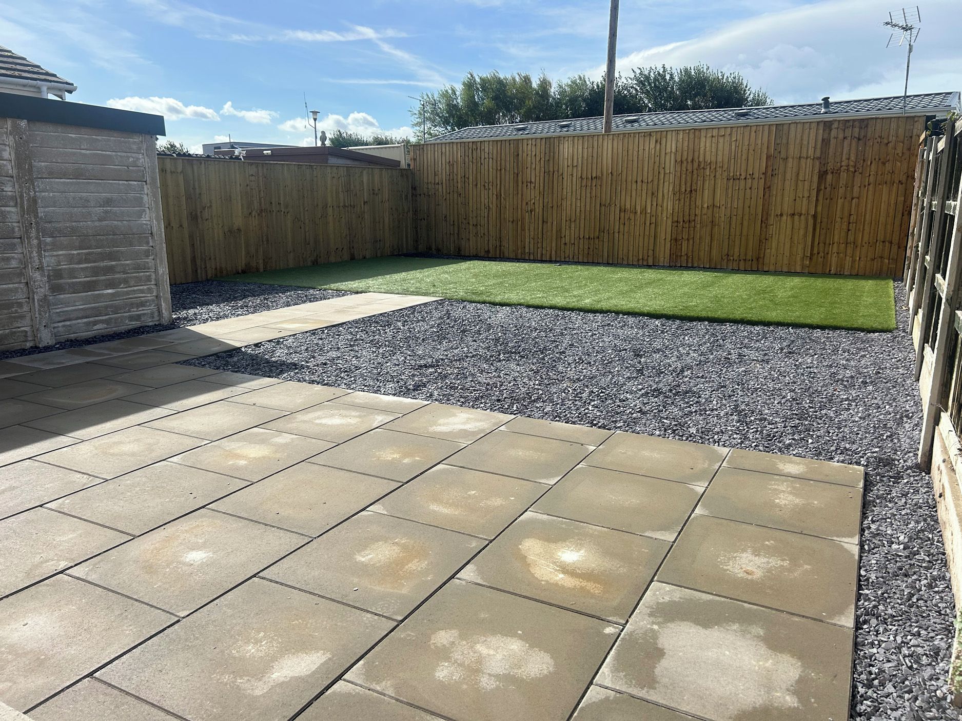 Un patio empedrado con césped y valla de madera.