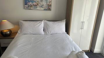 A hotel room with a bed, a nightstand with a lamp, a wardrobe, and a painting on the wall.