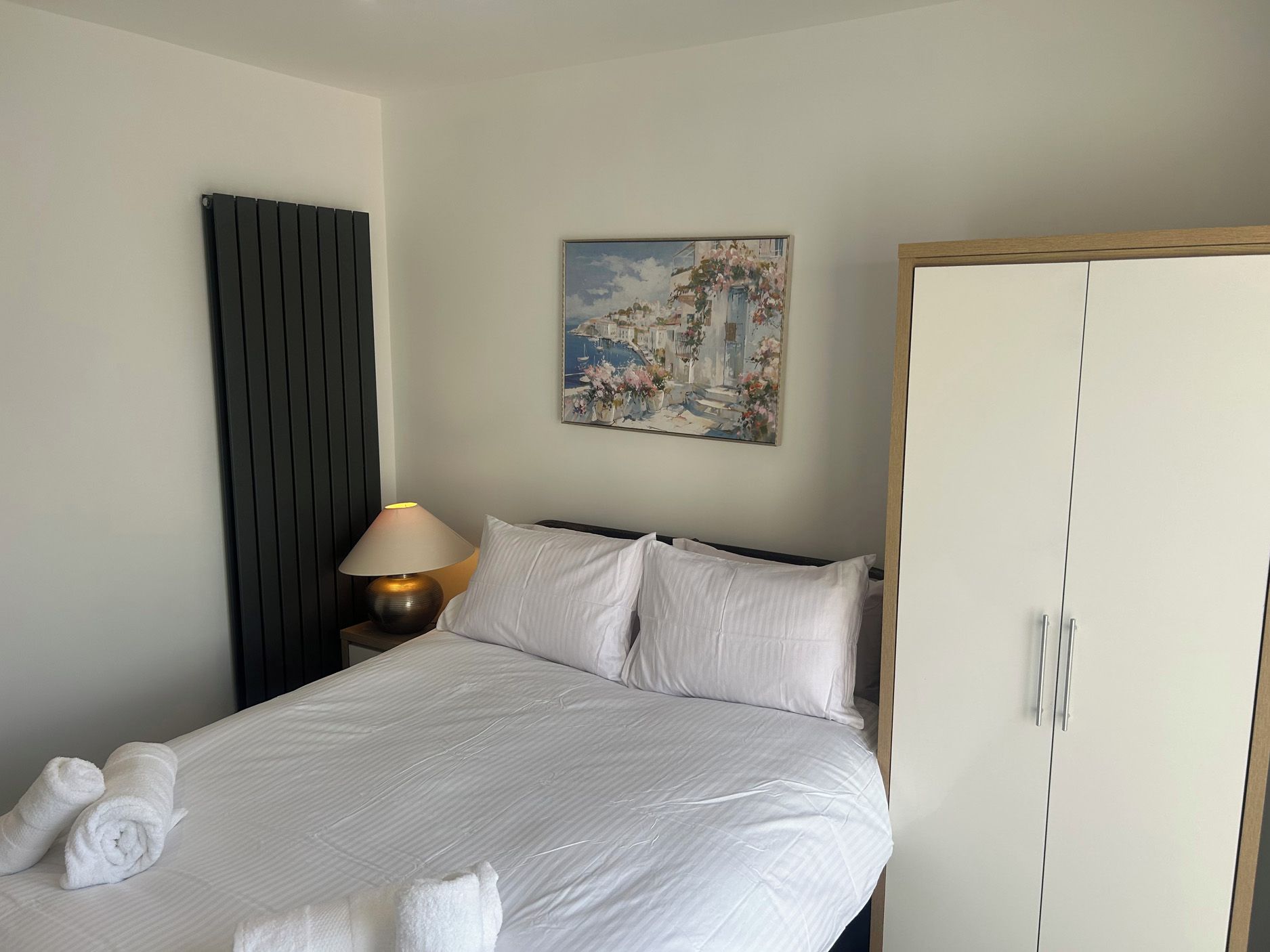 Et hotelværelse med en seng, et natbord med lampe, et klædeskab og et billede på væggen.