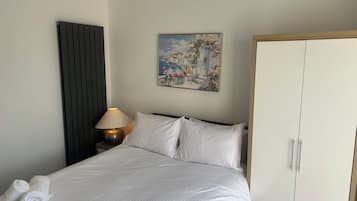 Et hotelværelse med en seng, et natbord med lampe, et klædeskab og et billede på væggen.