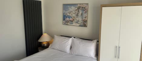 Una habitación de hotel con cama, lámpara de noche, un cuadro y un armario.