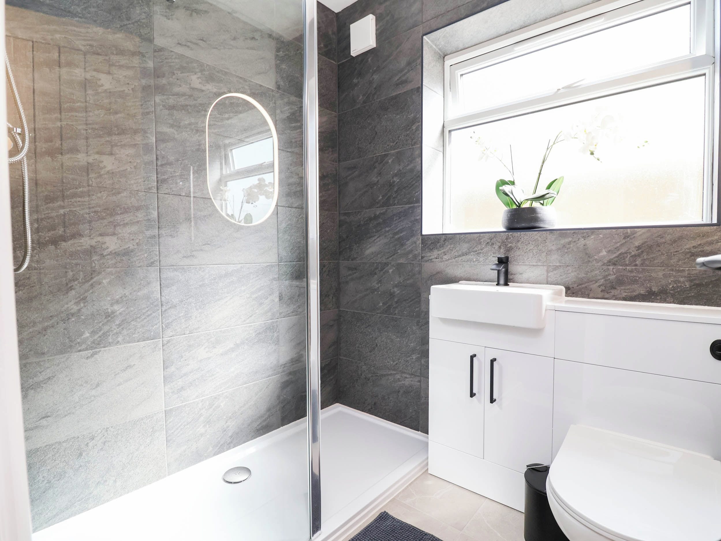 Un baño moderno con ducha envuelta en cristal, un lavamanos blanco y un inodoro.