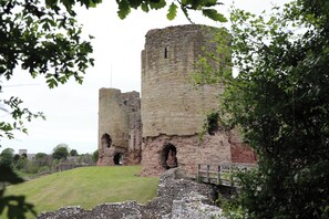 A historic stone castle with two prominent towers, a grassy foreground, and a wooden bridge. - 6 Bastion Close (Prestatyn)