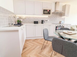 Cocina moderna con armarios blancos, microondas, hervidor y mesa de vidrio con sillas.