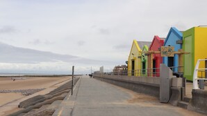 Un paseo marítimo junto a la playa con edificios de colores, arena y un camino de hormigón.