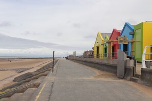 Un paseo marítimo junto a la playa con edificios de colores, arena y un camino de hormigón.