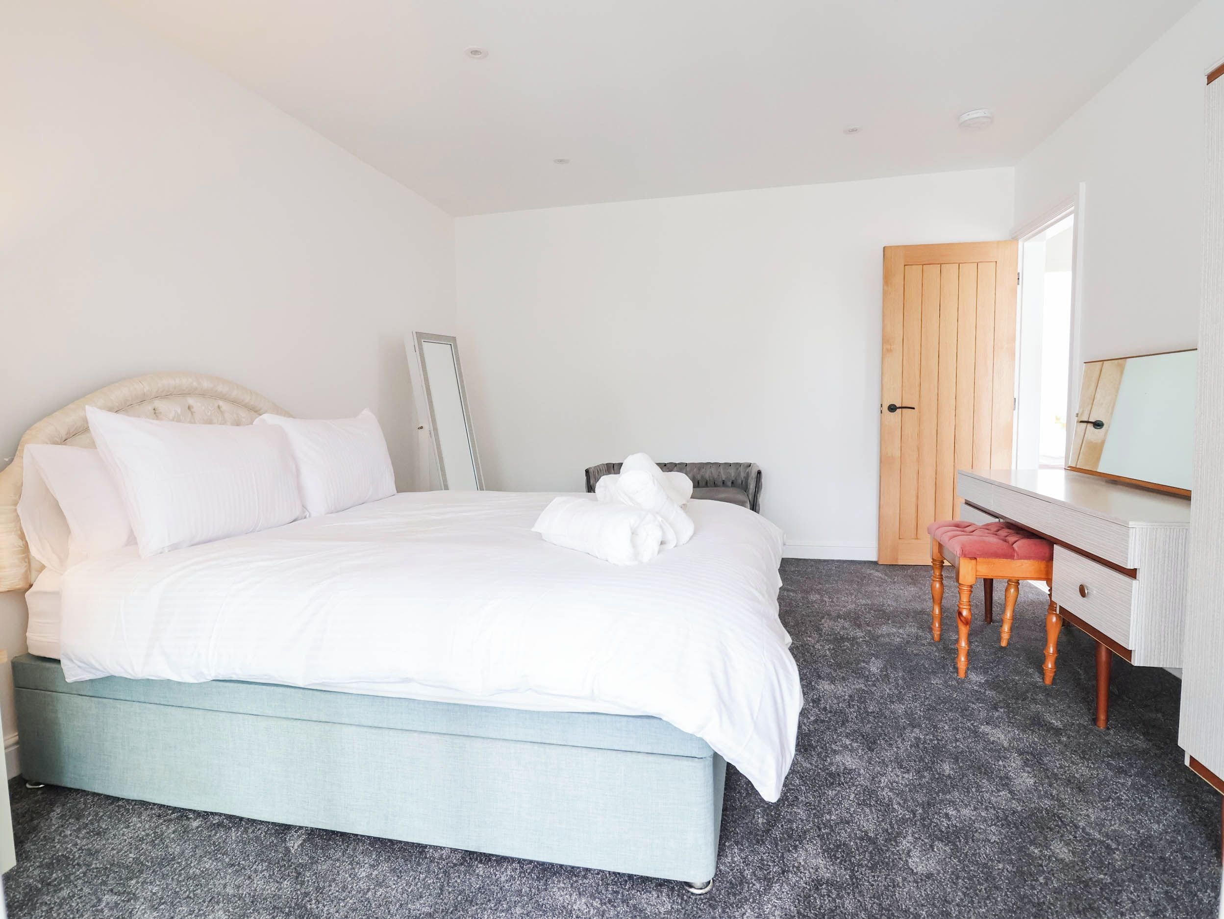 A bedroom with a bed, a bedside table, a chair, a mirror, and a door.