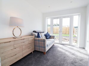 A room with a plaid sofa, a wooden dresser, and a lamp. There is a sliding glass door leading to an outdoor area. - 6 Bastion Close (Prestatyn)