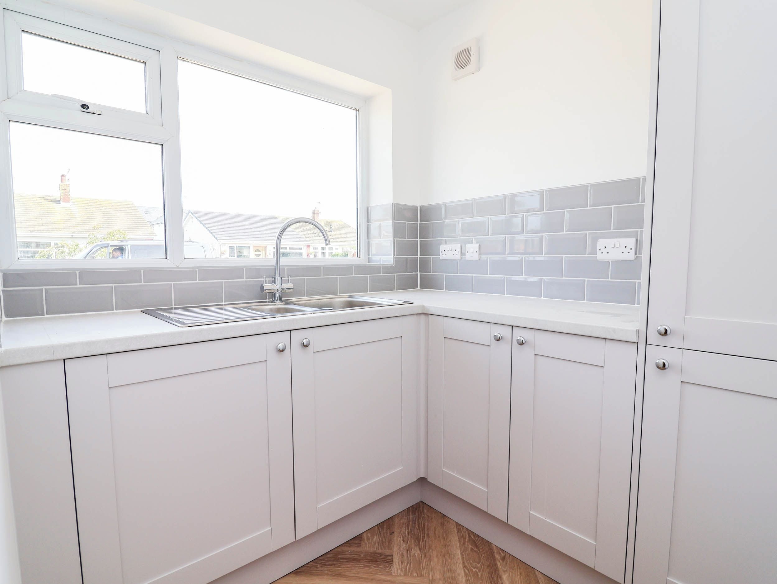 A kitchen with white cabinets, a window, and a grey backsplash.