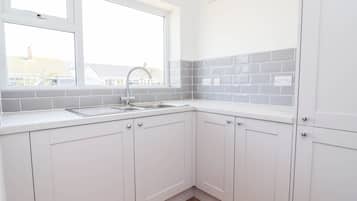 A kitchen with white cabinets, a window, and a grey backsplash.