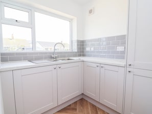 A kitchen with white cabinets, a window, and a grey backsplash. - 6 Bastion Close (Prestatyn)