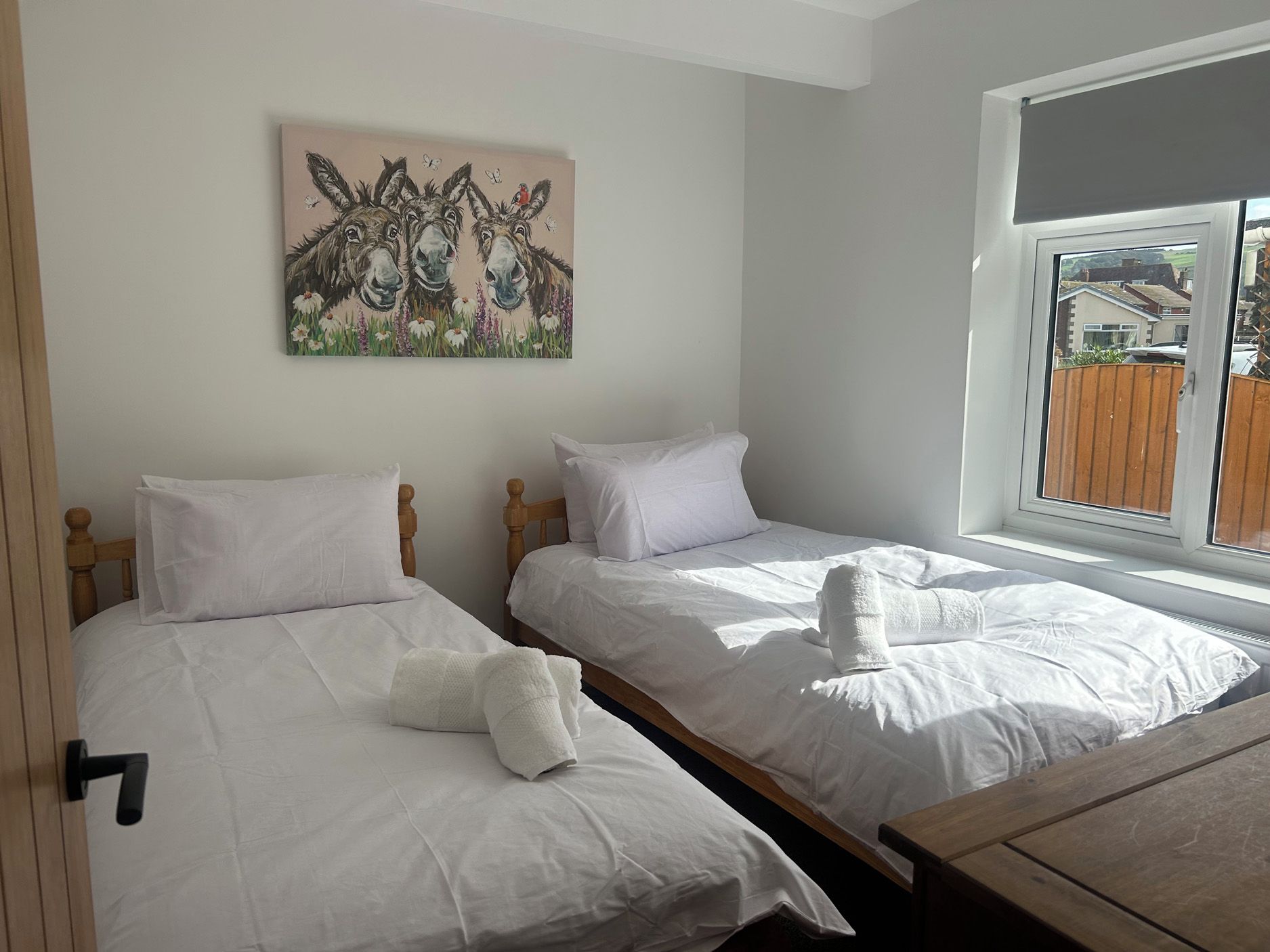 Un dormitorio con dos camas individuales, cabecera de madera, ropa de cama blanca y un cuadro de animales en la pared.