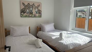 Un dormitorio con dos camas individuales, cabecera de madera, ropa de cama blanca y un cuadro de animales en la pared.
