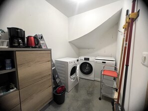 Ein Waschraum mit Waschmaschine, Trockner und einem kleinen Wäschewagen.