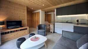 Un intérieur moderne avec un plafond en bois, un téléviseur à écran plat, un coin repas avec une table et des chaises, un canapé et une kitchenette.