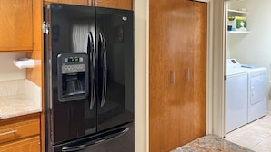 Une cuisine avec un réfrigérateur noir, des armoires en bois, un plan de travail en marbre et un coin buanderie équipé d’une machine à laver.