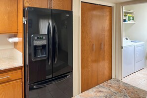 Eine Küche mit einem schwarzen Kühlschrank, Holzschränken, einer Marmorarbeitsplatte und einer Waschküche inklusive Waschmaschine.