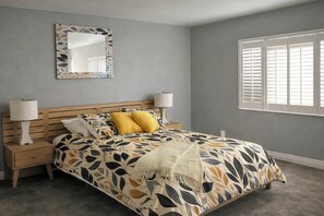 Ein Schlafzimmer mit einem Bett, zwei Nachttischen, einem Schminktisch und einem Spiegel, sowie einem Fenster mit Jalousien.