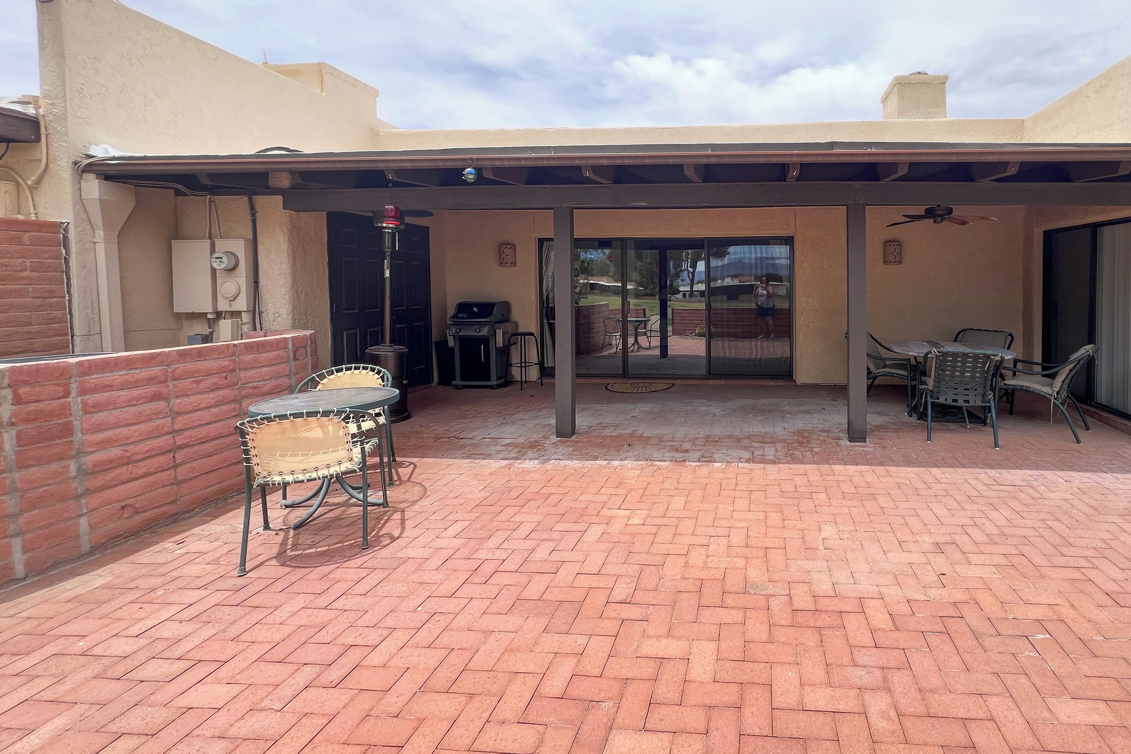 Un patio exterior con suelo de ladrillo, zona de estar cubierta y una parrilla.