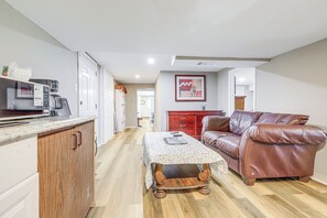 A kitchen with a microwave, coffee maker, and a wooden cabinet. There is a dining table with a floral tablecloth and a brown leather couch. A red cabinet and a framed picture are also visible. - Near Southern Regional MC! Commuter-Friendly Base (Riverdale)
