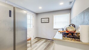 Una cocina con refrigerador de acero inoxidable, encimera de madera, ventana con persianas y el texto 'FAITH' enmarcado en la pared.