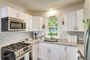 Una cocina con alacenas blancas, una estufa de acero inoxidable, un microondas y una ventana con vistas a zonas verdes.