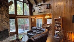 Ein gemütliches Blockhaushaus-Interieur mit Kamin aus Stein, Ledersofa, Essbereich und großen Fenstern.