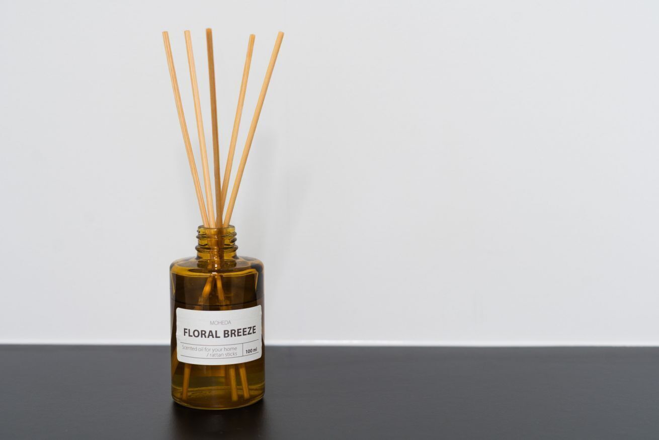 Um frasco de óleo perfumado com palitos de junco, rotulado 'MOREDA FLORAL BREEZE,' sobre uma superfície preta contra um fundo branco.