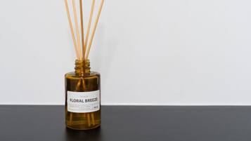 Um frasco de óleo perfumado com palitos de junco, rotulado 'MOREDA FLORAL BREEZE,' sobre uma superfície preta contra um fundo branco.