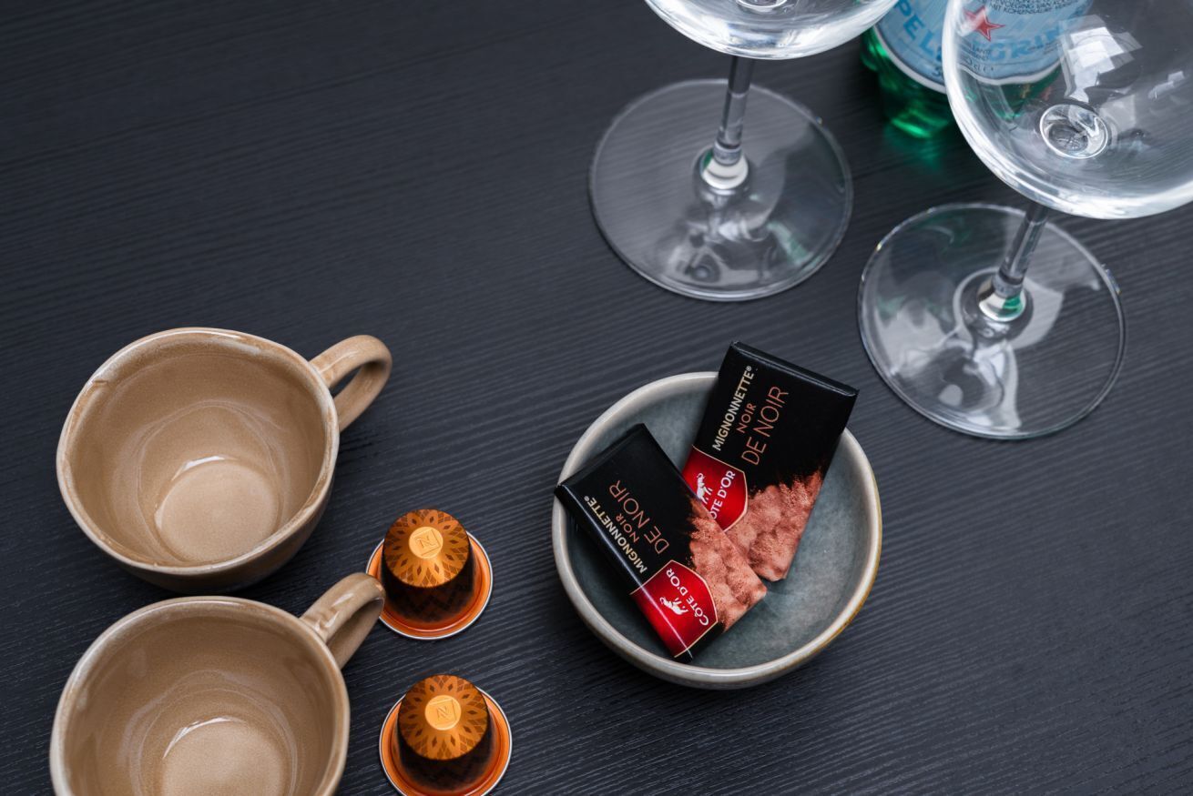 A table with two mugs, a plate with chocolate bars, and two wine glasses.