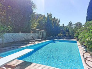 Ein Swimmingpool mit Liegestühlen, umgeben von Steinmauern und Bäumen.