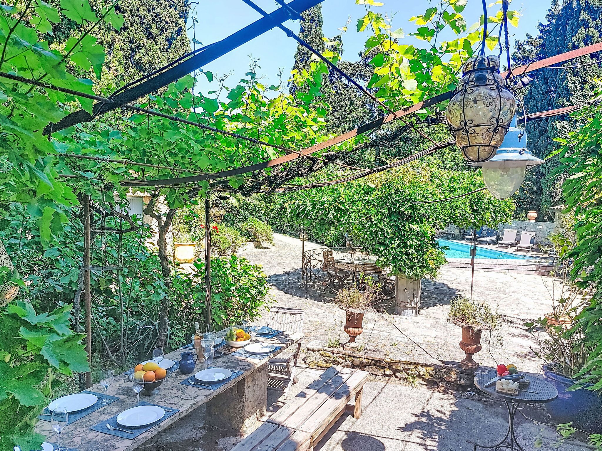 Een buiten eetgedeelte met een zwembad, omringd door groen en een pergola.