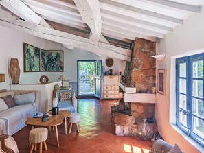 Ein gemütliches Wohnzimmer mit einer Couch, einem Couchtisch und einem Essbereich mit Stühlen. Eine Steinwand und eine Holzbalkendecke runden den Raum ab.