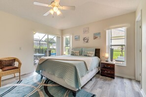 Ein Schlafzimmer mit Bett, Stuhl, Nachttisch, Fenster und Deckenventilator.