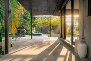 Et overdækket udendørsområde med pool, siddepladser og tropiske planter.