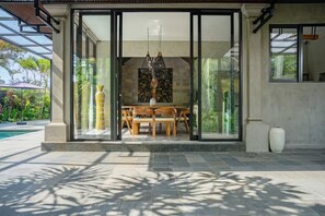 A modern house with a glass door leading to an outdoor dining area with a table and chairs. - Kokokan Villa Ubud (Gianyar)