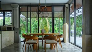 A modern kitchen with a dining area, large windows, and a view of greenery. - Kokokan Villa Ubud (Gianyar)