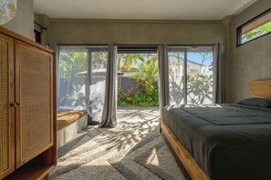 A bedroom with a bed, a rattan wardrobe, and a view of a garden through a sliding door. - Kokokan Villa Ubud (Gianyar)