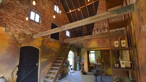 Um interior rústico com paredes de tijolo aparente, uma escada de madeira e uma área de estar com cadeiras e estantes.