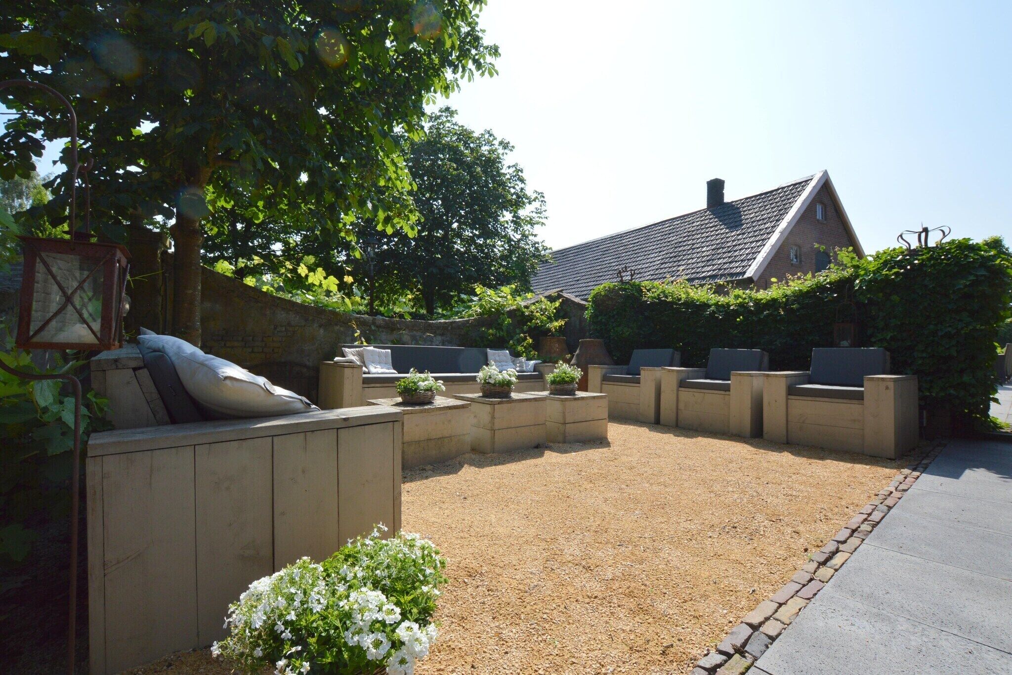 A garden patio with outdoor seating, a stone wall, and a house in the background.