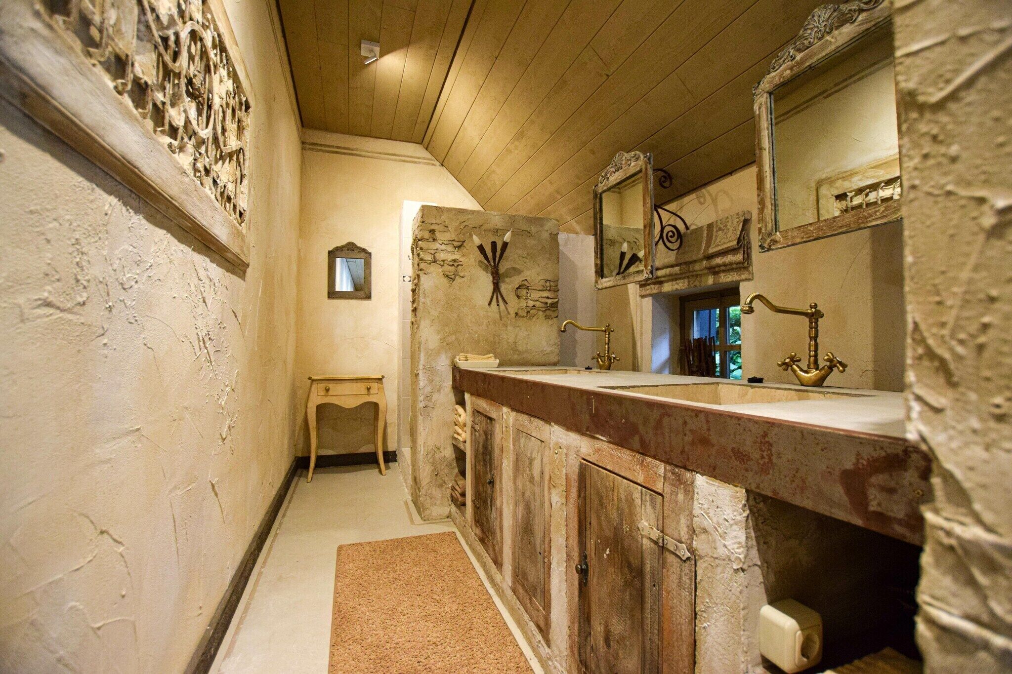 A bathroom with a wooden ceiling, stone wall, and a large mirror.