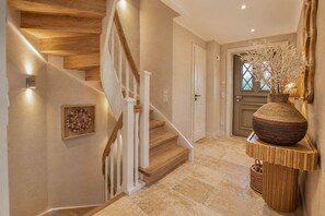 Eine Treppe mit Holzboden und weißen Geländern, eine Tür mit einem verzierten Fenster und eine große Vase auf einem Holztisch.