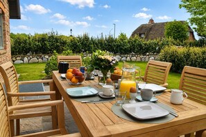 Ein Holztisch, gedeckt für das Frühstück, mit Tellern, Gläsern und einer Obstschale.