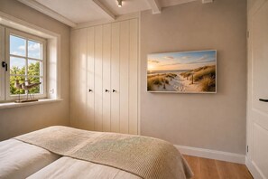 Ein Schlafzimmer mit einem Bett, einem Fenster mit Vögeln, einem Kleiderschrank und einem Strandbild.